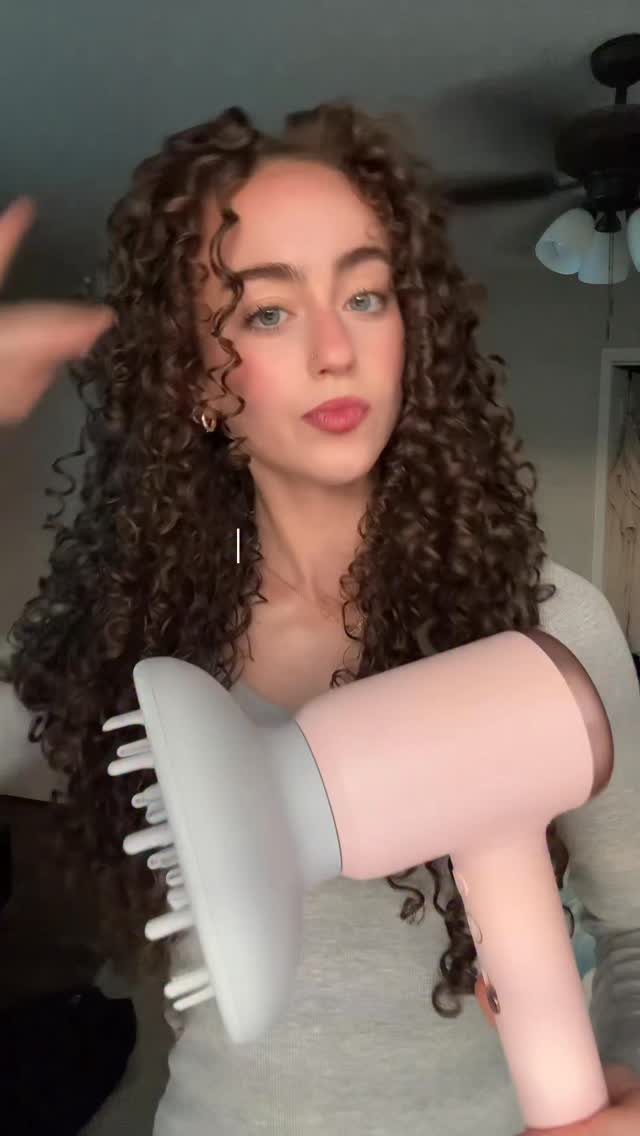 2C Curly Hairstyles: 10 Ideas for Layers, Buns and Bangs 2 Woman with curly brown hair holding a pink hair dryer with white diffuser attachment