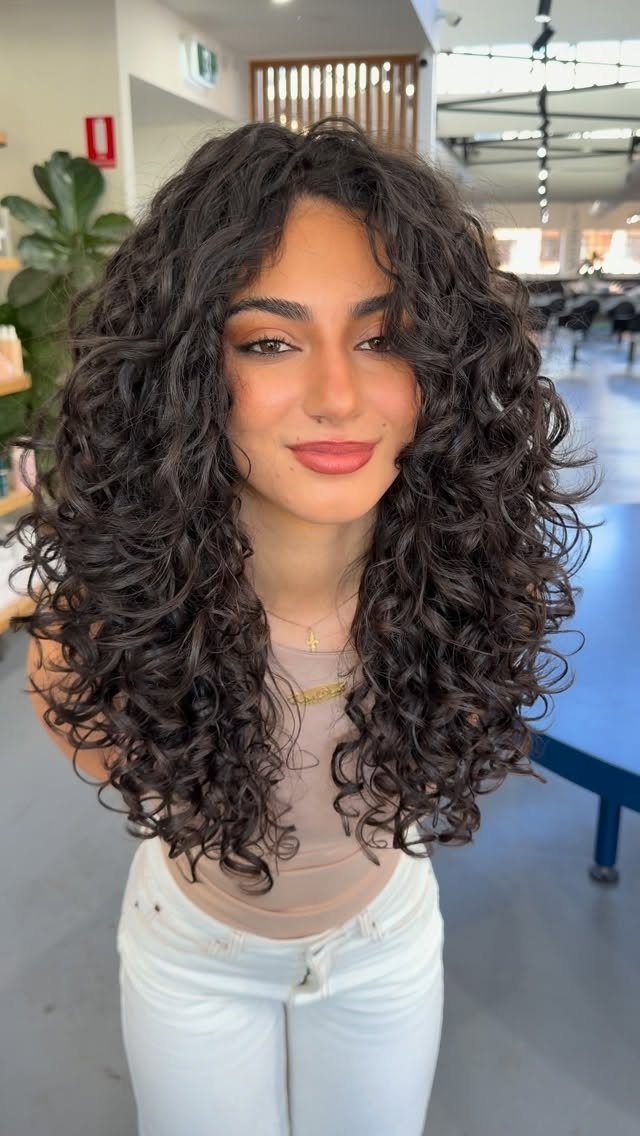 2C Curly Hairstyles: 10 Ideas for Layers, Buns and Bangs 1 Woman with voluminous dark brown curly hair styled in a layered haircut.