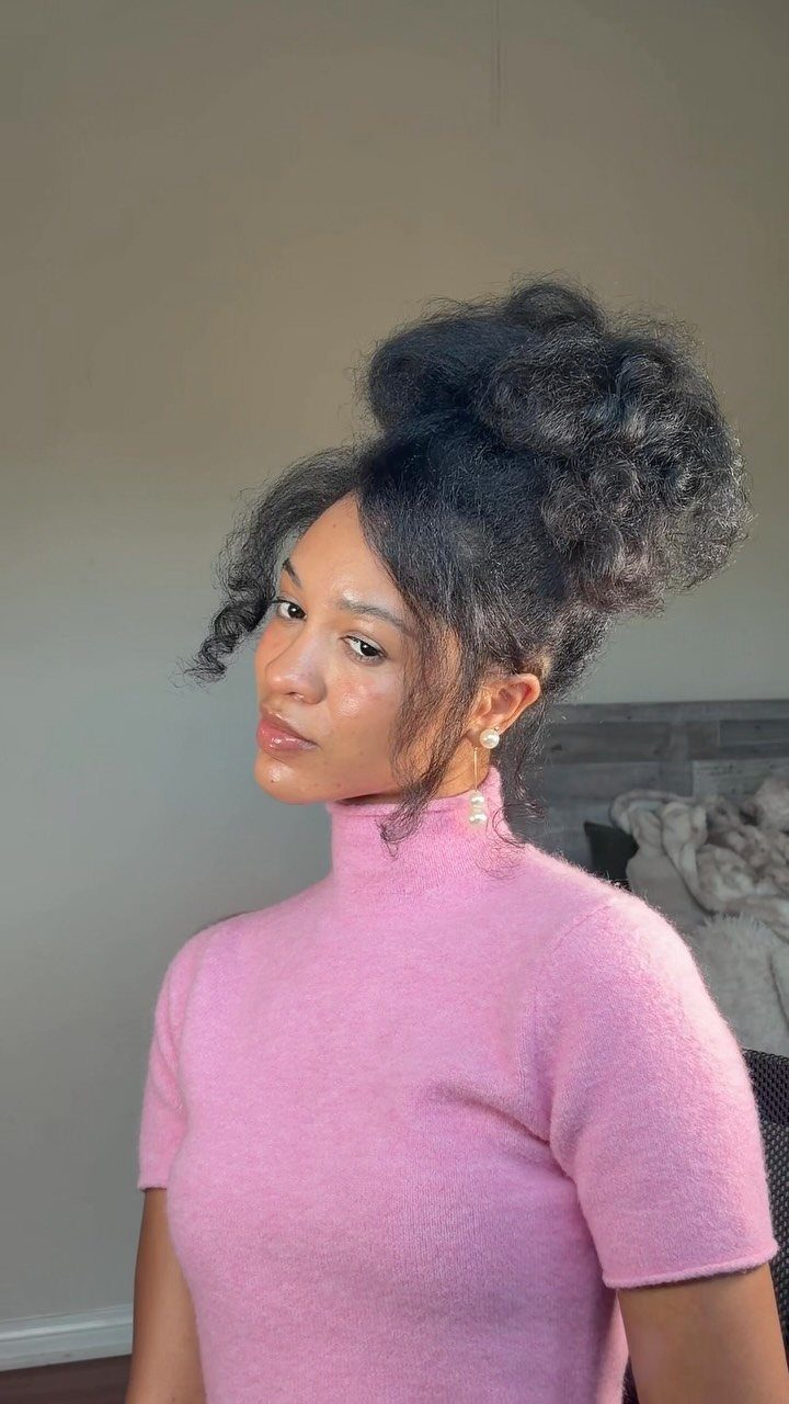 4C Hair Blown Out with Braids, Buns and Waves: 9 Ideas 7 Woman with voluminous 4C hair in a high bun wearing a pink turtleneck.