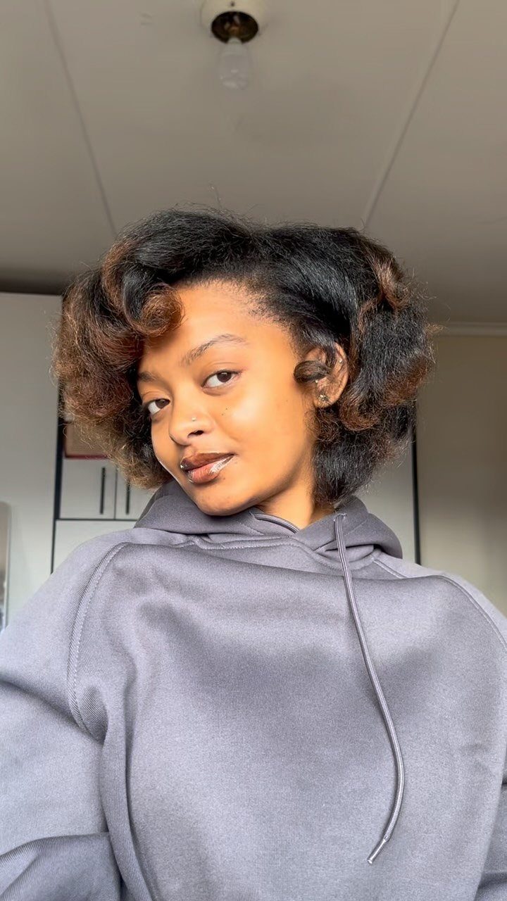 Woman with voluminous blow-dried natural hair wearing a grey hooded sweatshirt indoors.