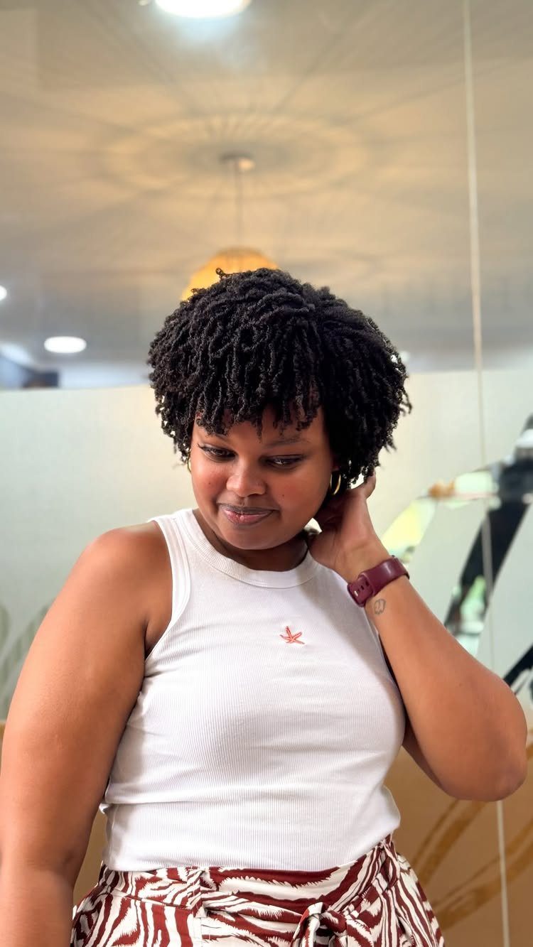 Woman with short, tightly coiled black finger coils wearing a white ribbed top.