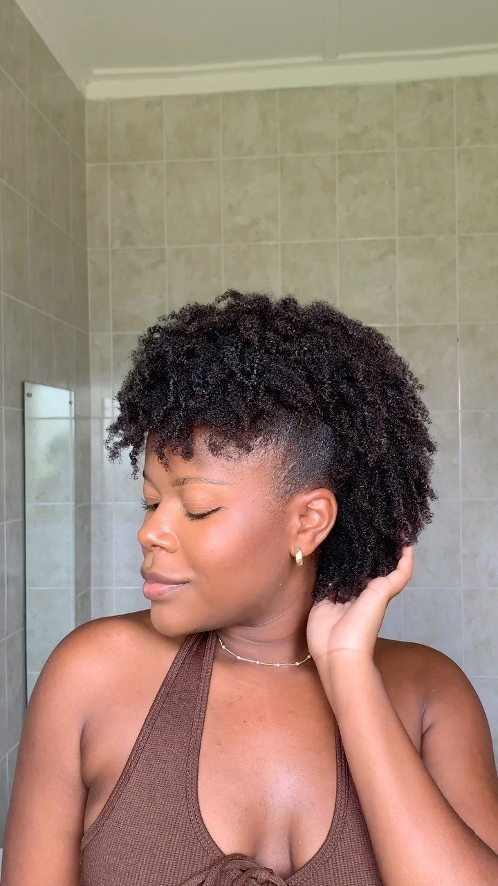 Woman with a curly frohawk hairstyle and shaved sides posing in a bathroom.