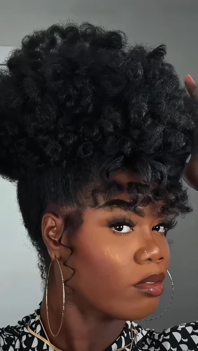 Woman with a large, curly high puff hairstyle and gold hoop earrings.