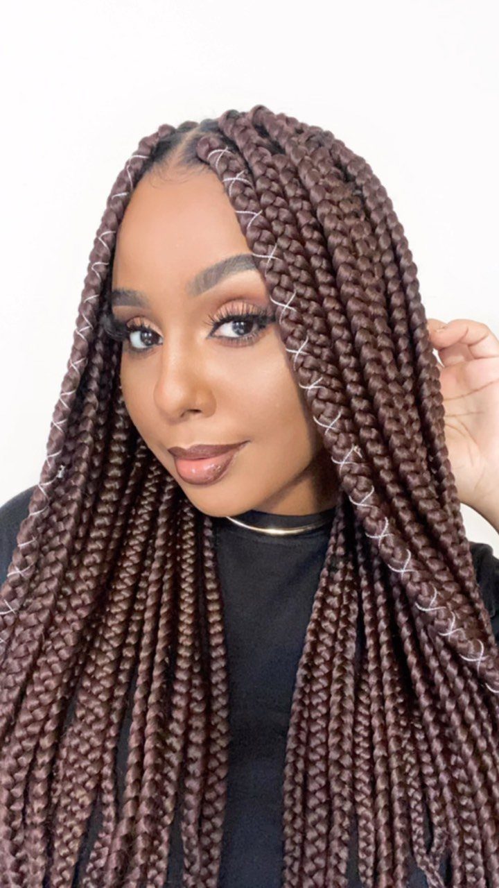 Woman with long reddish-brown jumbo box braids posing against a white background.