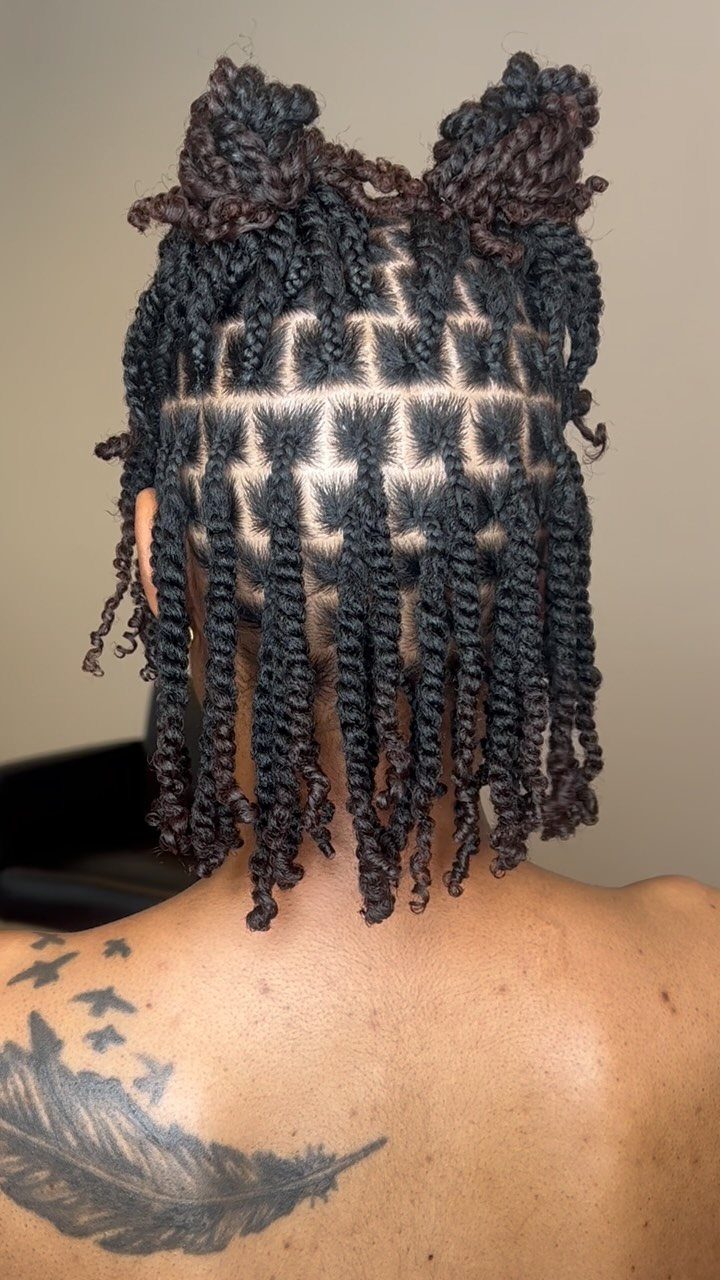 Two-strand twists on natural hair with two small buns on top and back tattoo.