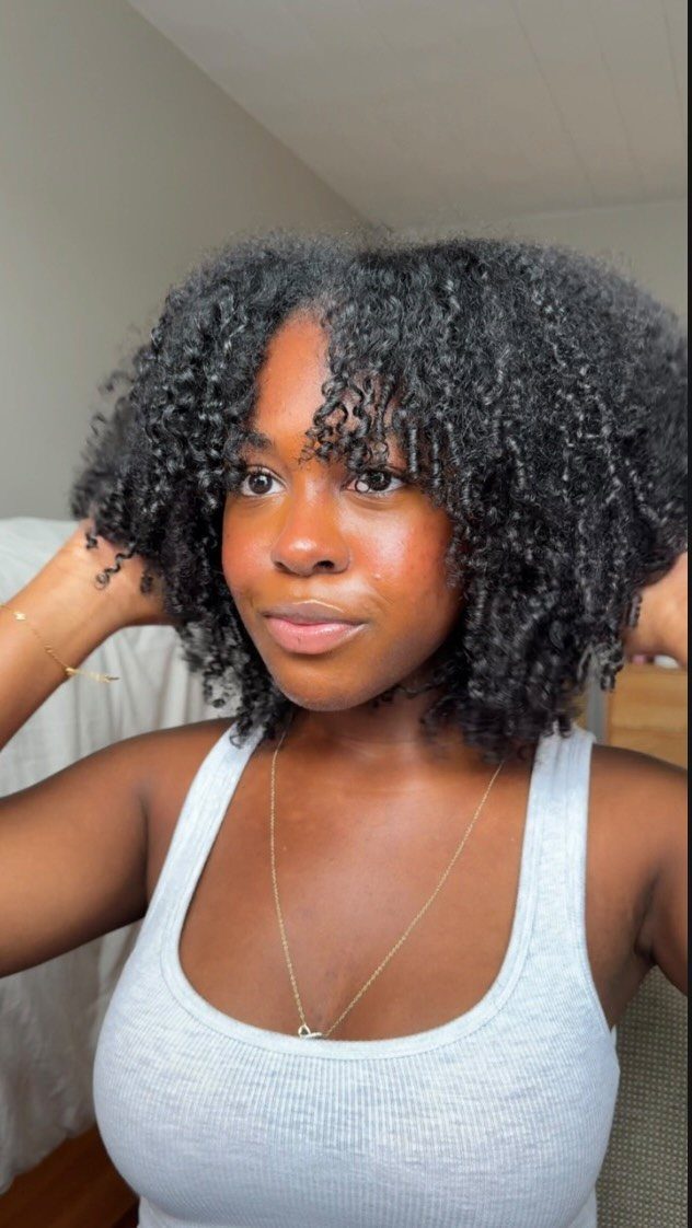 Woman with voluminous curly black natural hair wearing a grey ribbed tank top.