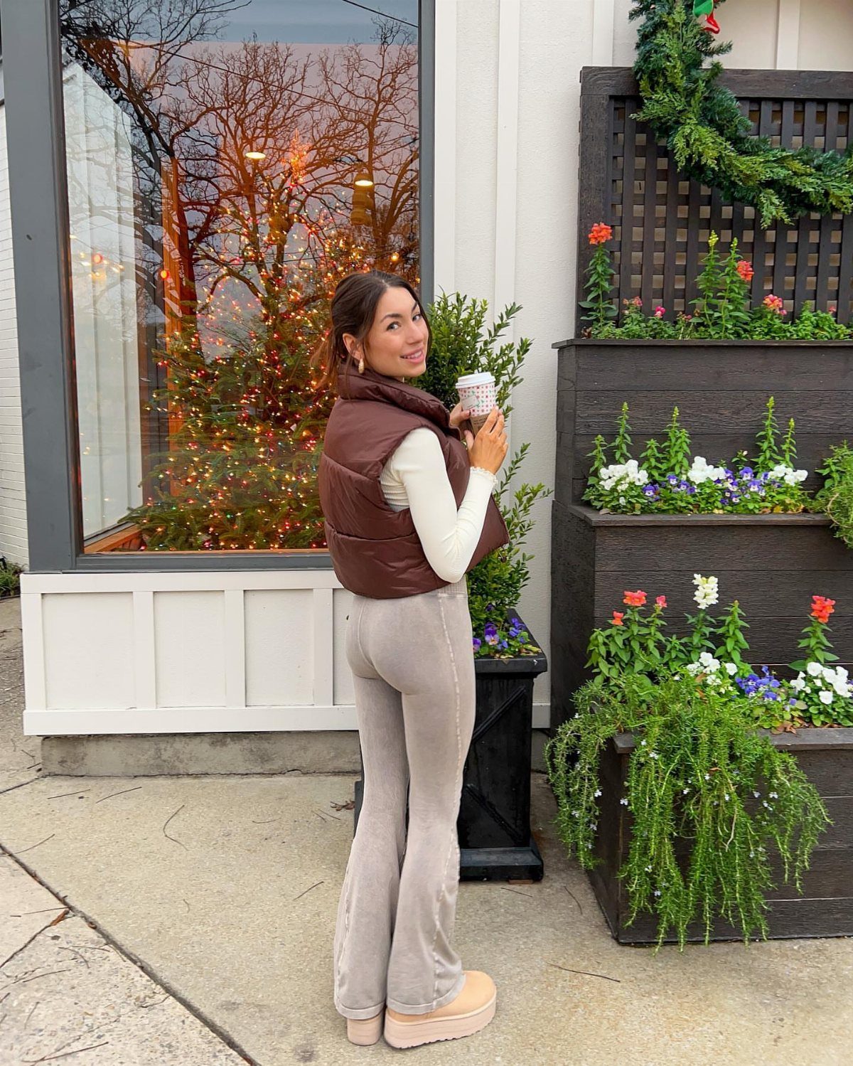 57 Degree Weather Outfit: 19 Ideas to Wear Now 14 Woman wearing a brown puffer vest and grey flared trousers holding a coffee cup.