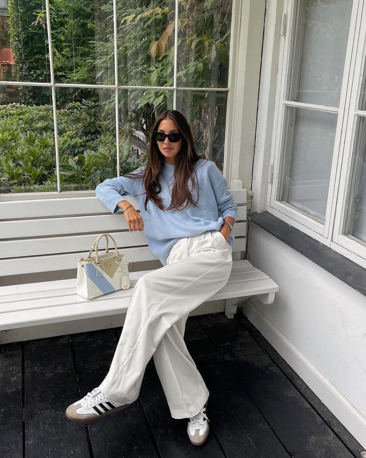 Woman in blue sweater and white trousers wearing grey Adidas Samba sneakers.