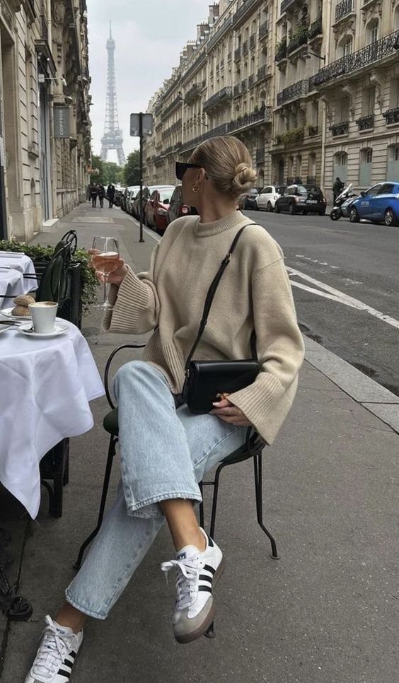 Woman in beige sweater and light blue jeans wearing grey Adidas Samba sneakers.