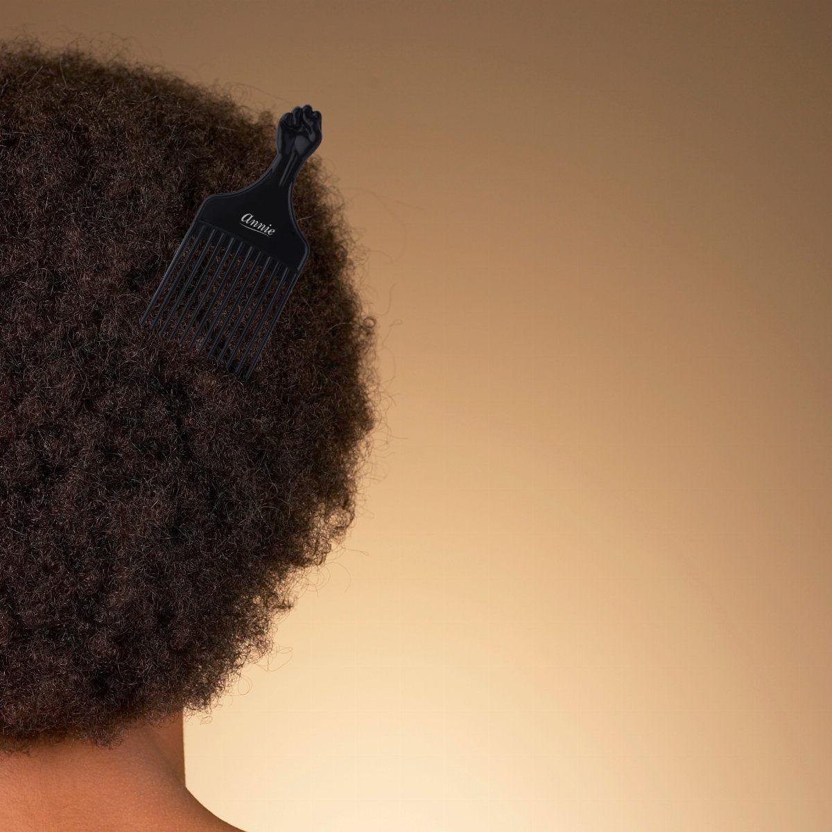 Black afro pick with raised fist handle inserted into curly afro hair.