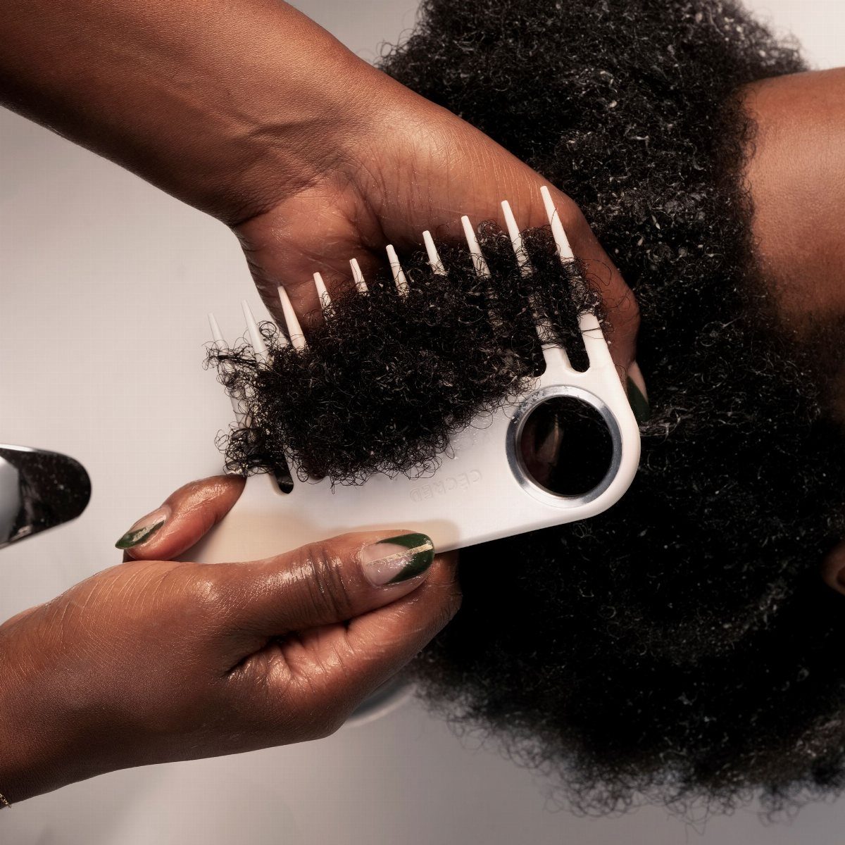 White wide-tooth comb detangling thick curly black hair held by two hands.