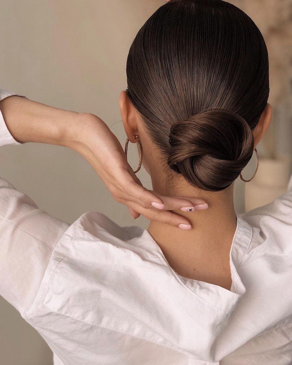 7 Back Hairstyle for Women Ideas, Braids to Buns 5 Woman with dark brown hair styled in a slicked-back low bun from behind.