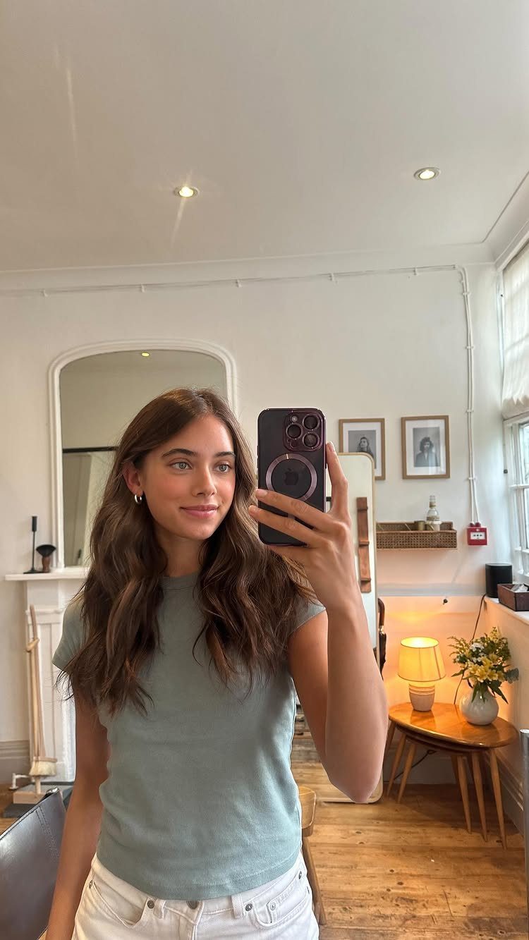 Best Hair Dye for Dark Hair: 8 Shades and Ideas 1 Woman with long wavy dark brown hair taking a mirror selfie in a room.