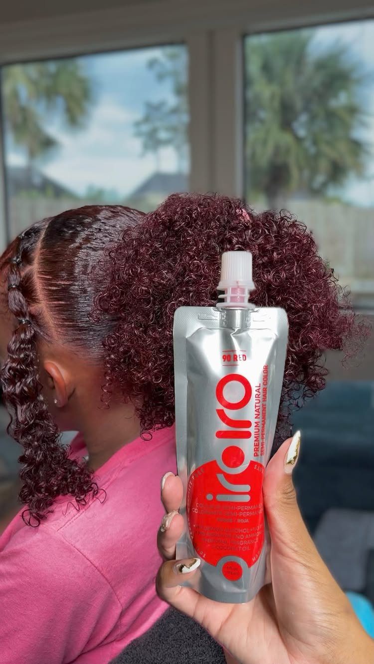 Best Hair Dye for Dark Hair: 8 Shades and Ideas 3 Person with curly burgundy hair holding a tube of hair dye product.