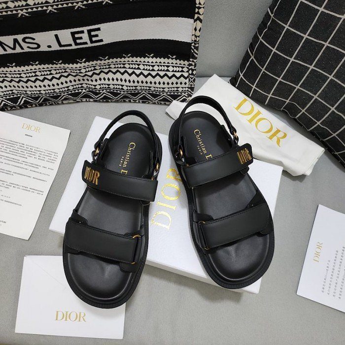 Black leather Dior sandals with gold lettering on a white branded box