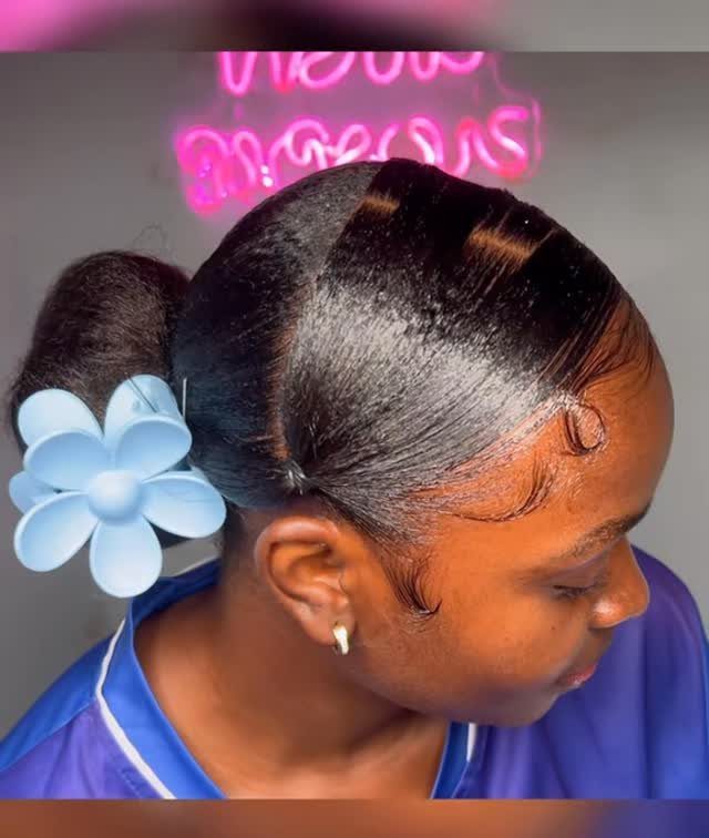 17 Black Natural Hair Ideas for Every Length and Style 2 Black woman with a sleek natural ponytail and a large blue flower accessory.