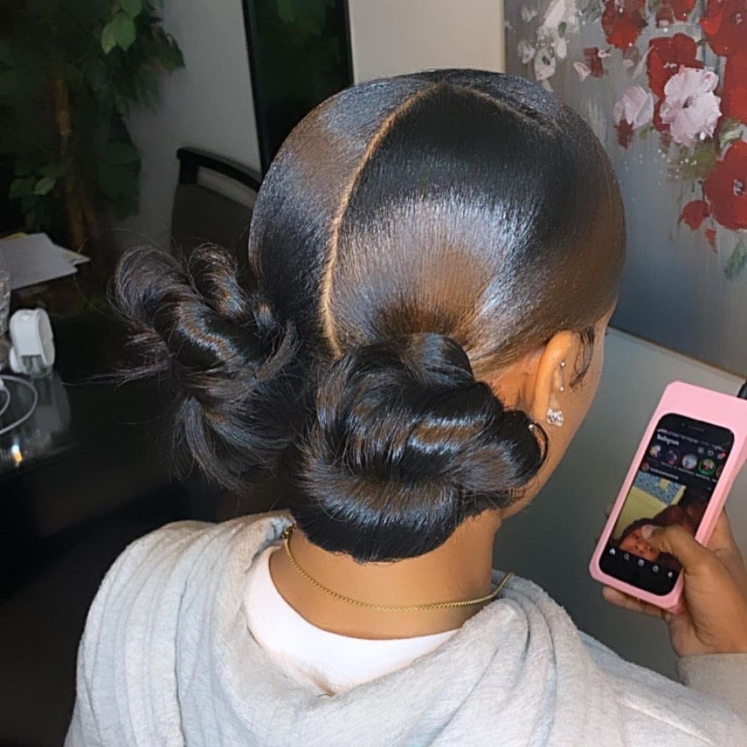 17 Black Natural Hair Ideas for Every Length and Style 10 Woman with sleek black hair styled into two space buns taking a selfie.