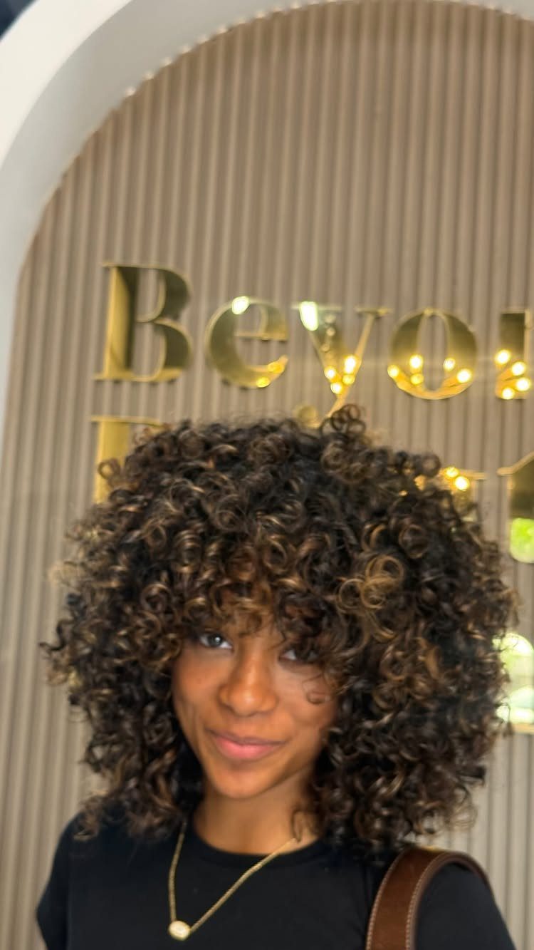 17 Black Natural Hair Ideas for Every Length and Style 15 Woman with voluminous ringlet afro hair and blonde highlights wearing a black shirt.