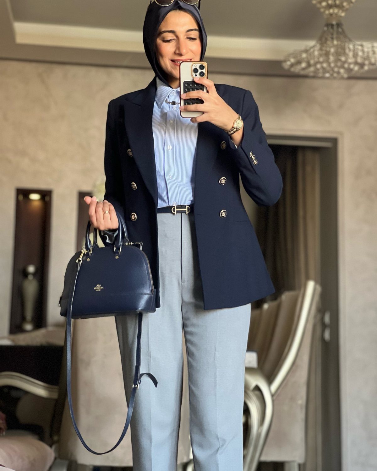 Blue Blazer Outfit for Women: 24 Ideas to Wear 23 Woman in a dark blue blazer, light grey trousers, and black hijab holding a handbag.