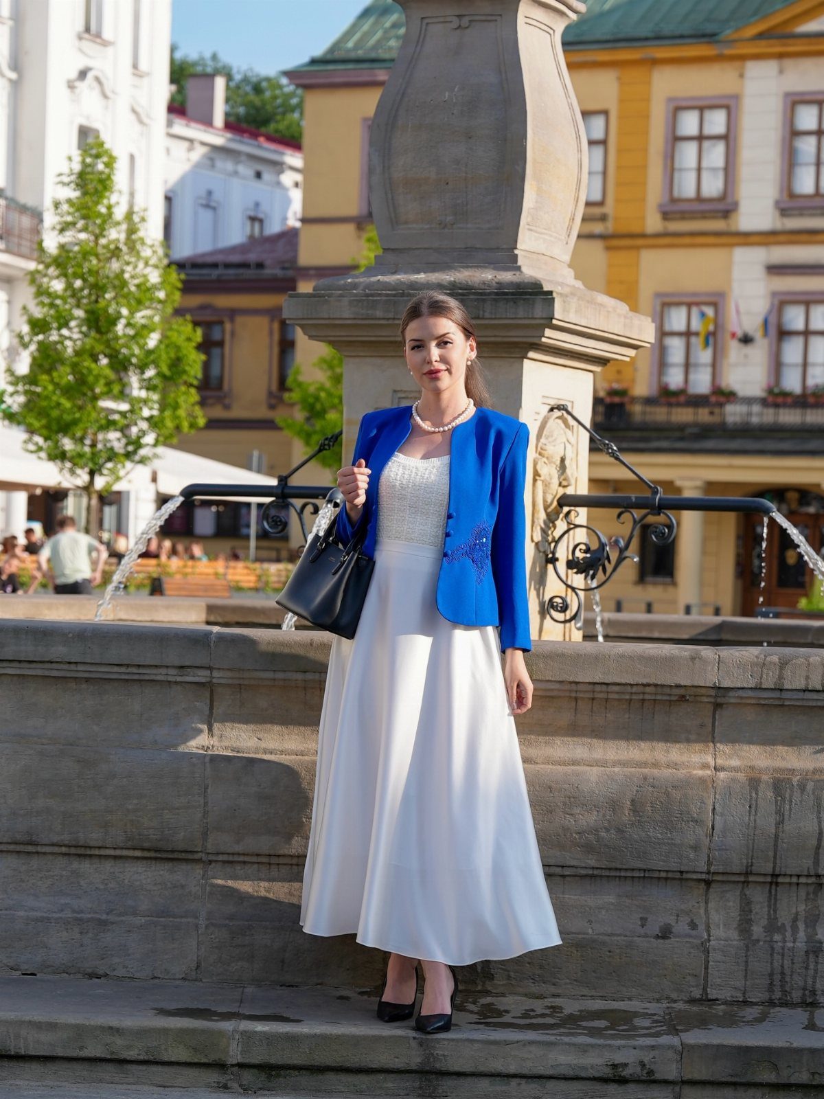 Blue Blazer Outfit for Women: 24 Ideas to Wear 6 Woman wearing a bright blue blazer over a long ivory dress by a fountain
