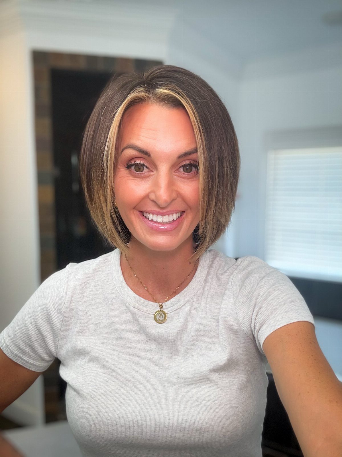 18 Bobo Hair Style Ideas, From Lob to Boxy Cuts 4 Woman with a chin-length brown bob haircut and blonde highlights smiling indoors.