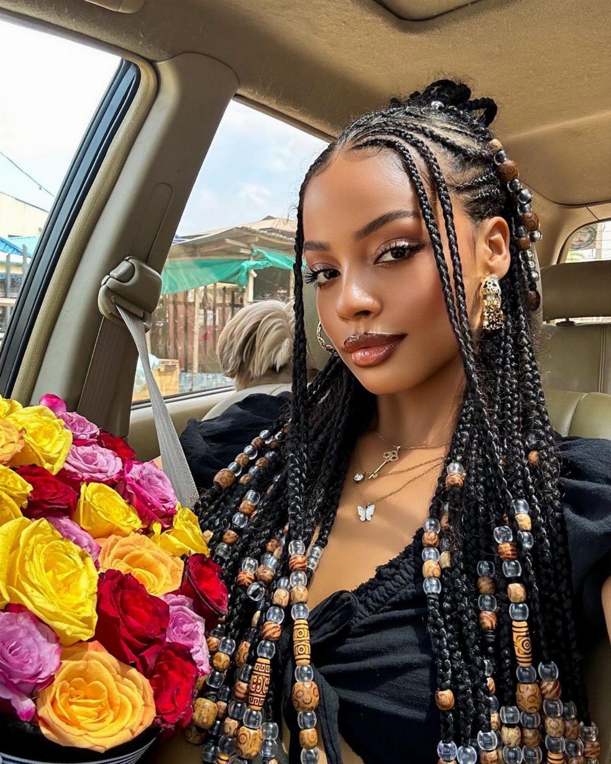 27 Boho Fulani Braids Hairstyles for Every Length and Look 3 Woman with beaded Fulani braids holding a colorful bouquet of roses in a car