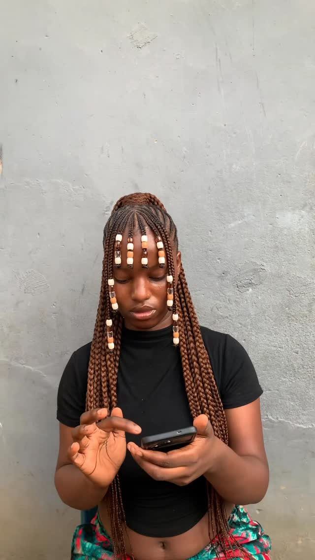 27 Boho Fulani Braids Hairstyles for Every Length and Look 20 Woman with brown Fulani braids and beaded bangs looking at her smartphone.