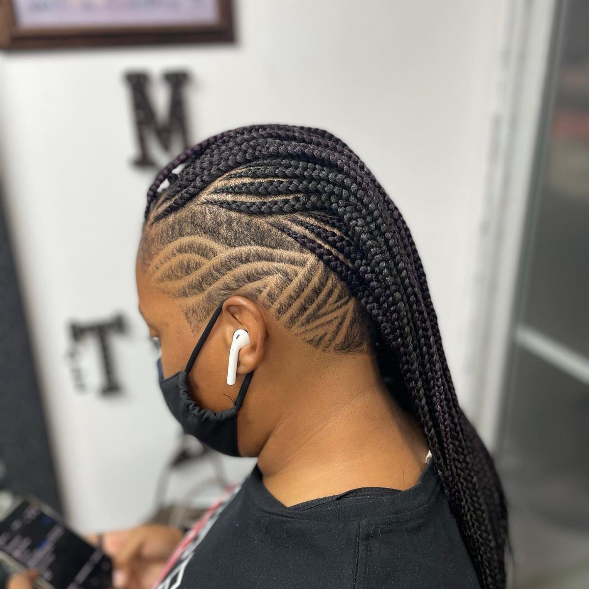 27 Boho Fulani Braids Hairstyles for Every Length and Look 16 Person with Fulani braids and shaved sides featuring artistic curved hair designs.