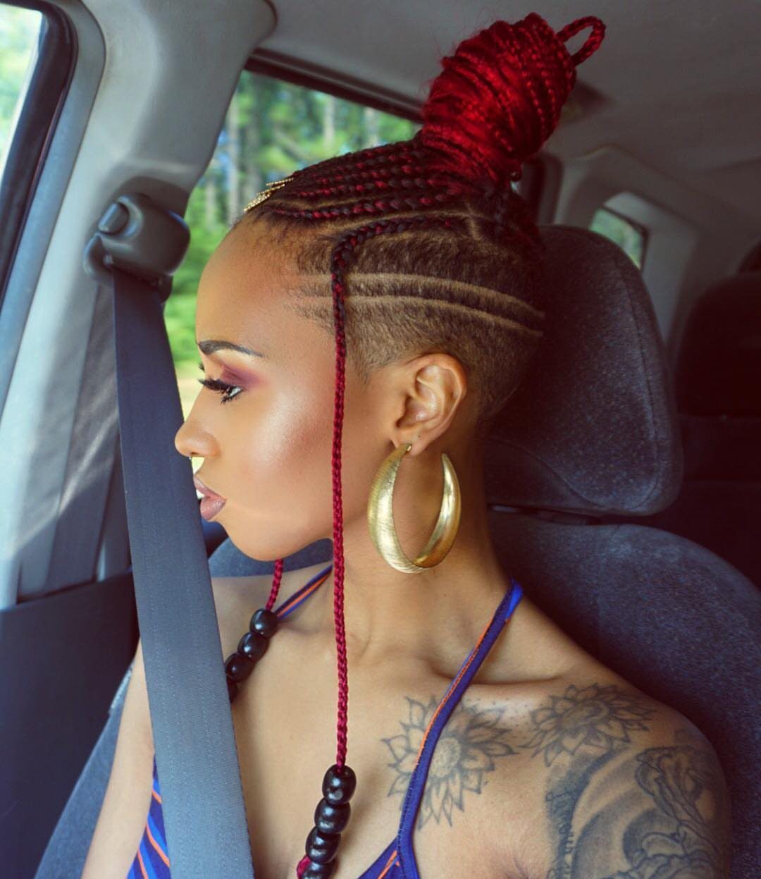 27 Boho Fulani Braids Hairstyles for Every Length and Look 12 Woman with red Fulani braids, a high bun, and shaved sides in a car