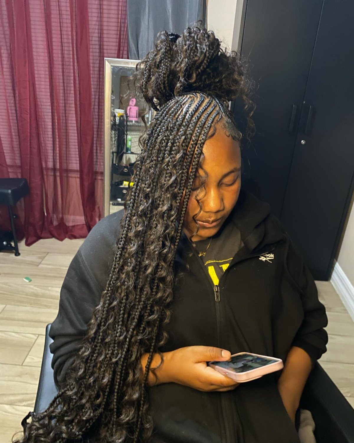 27 Boho Fulani Braids Hairstyles for Every Length and Look 2 Woman with long dark Fulani braids styled in a half top knot holding phone