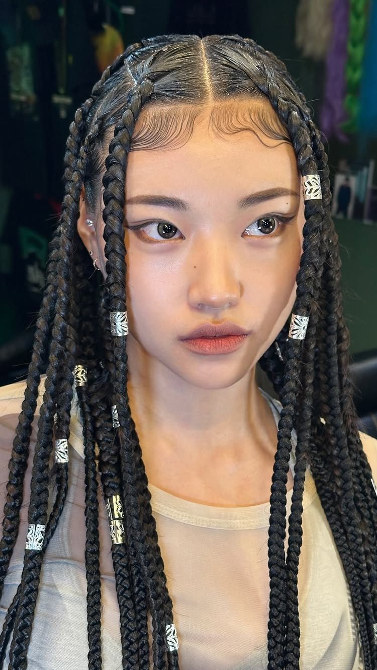 Woman with long black chunky box braids decorated with silver metallic hair cuffs.