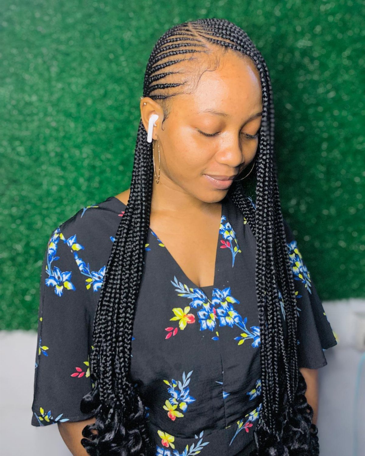 Woman with long black box braids and curled ends wearing a floral dress.