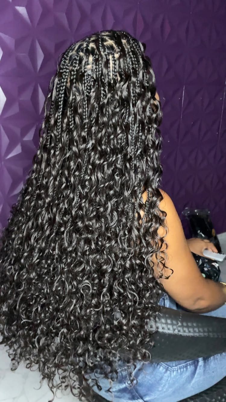 Long black box braids with curly loose ends against a purple textured wall