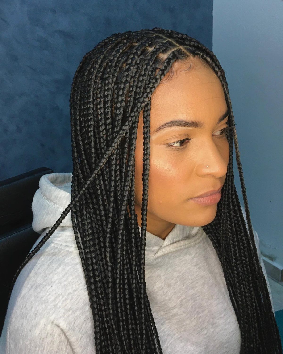 Woman with long black classic box braids wearing a grey hooded sweatshirt.