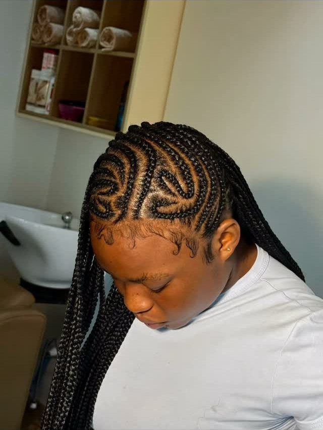 Person with black box braids and intricate curved parting patterns in a salon.