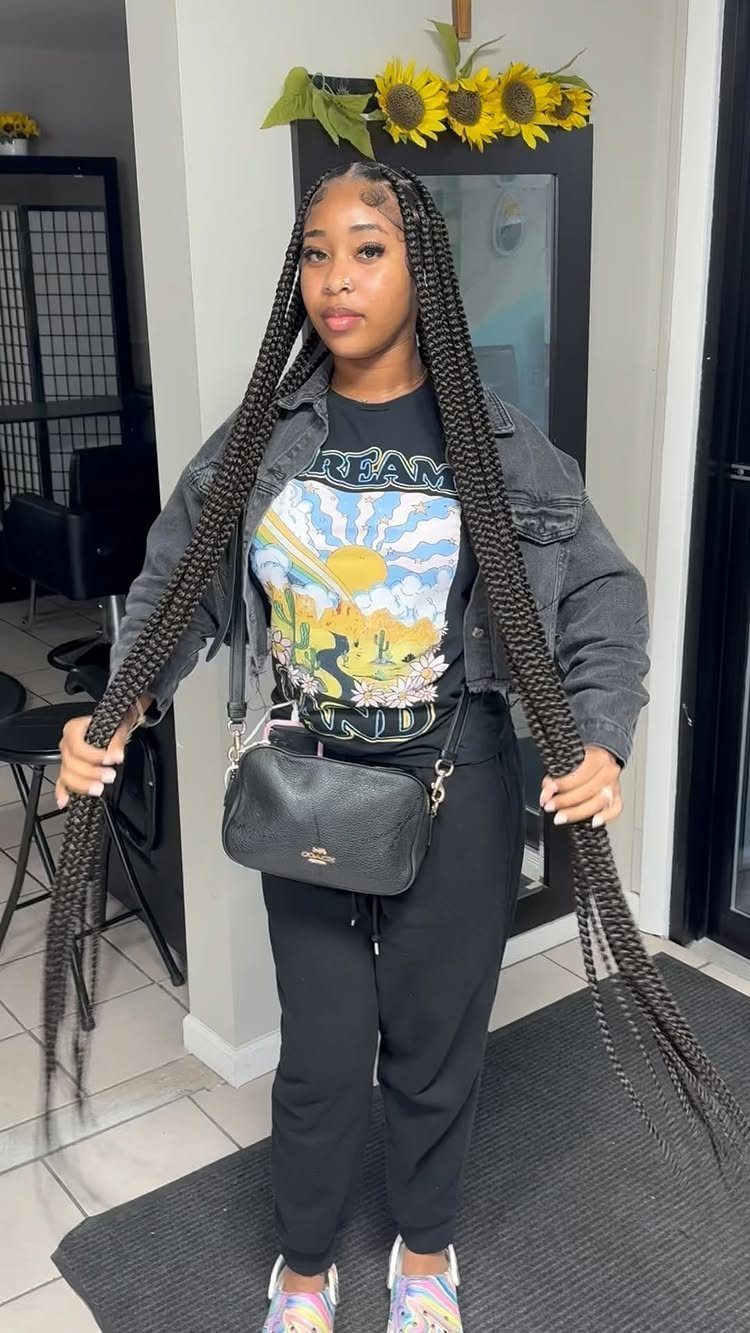 Woman with long, thick black jumbo box braids wearing a grey denim jacket.