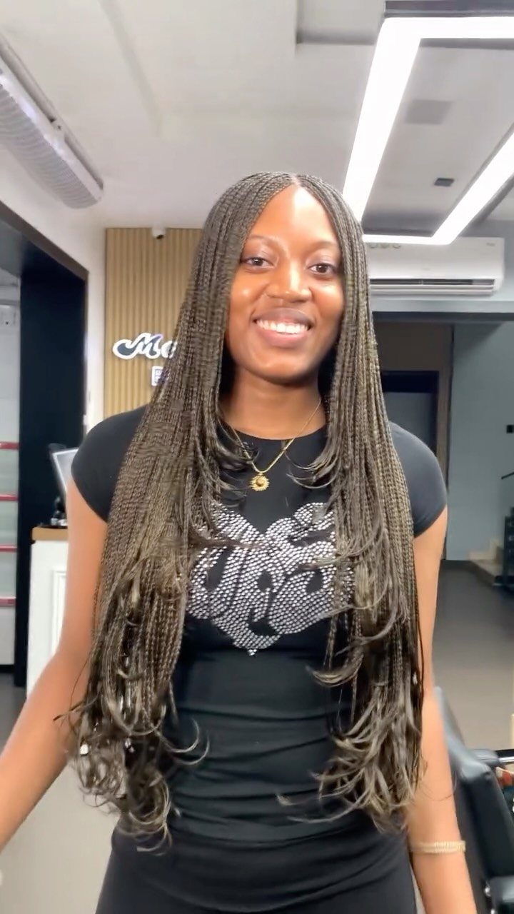 Woman with long brown layered box braids smiling in a bright hair salon.