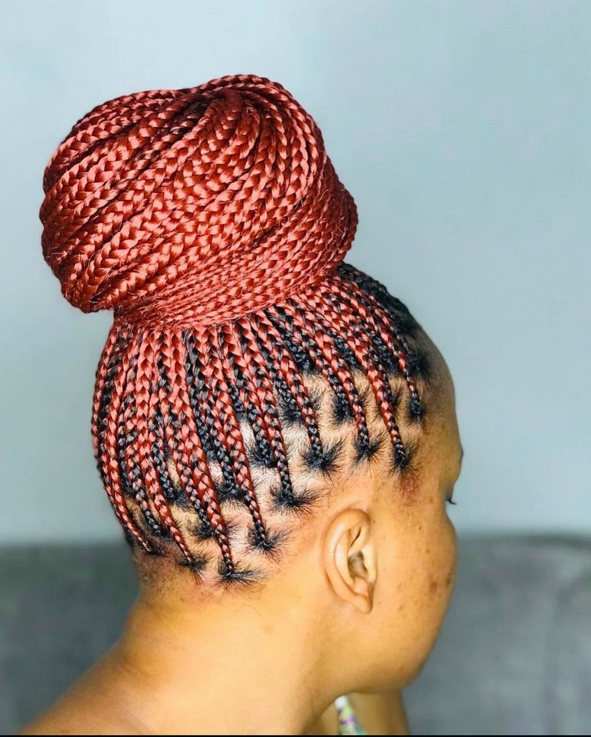 Reddish-brown box braids styled into a high, sleek top knot bun updo.