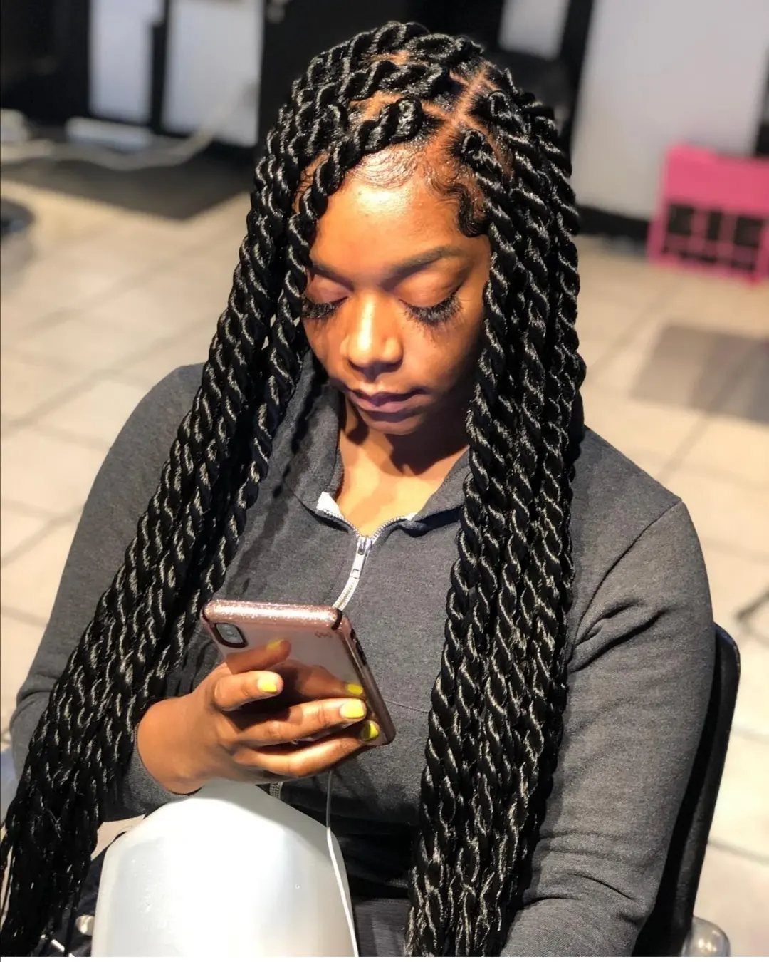 20 Braids and Women Hairstyles to Try in 2026 18 Woman with long black rope braids looking at her gold smartphone indoors.