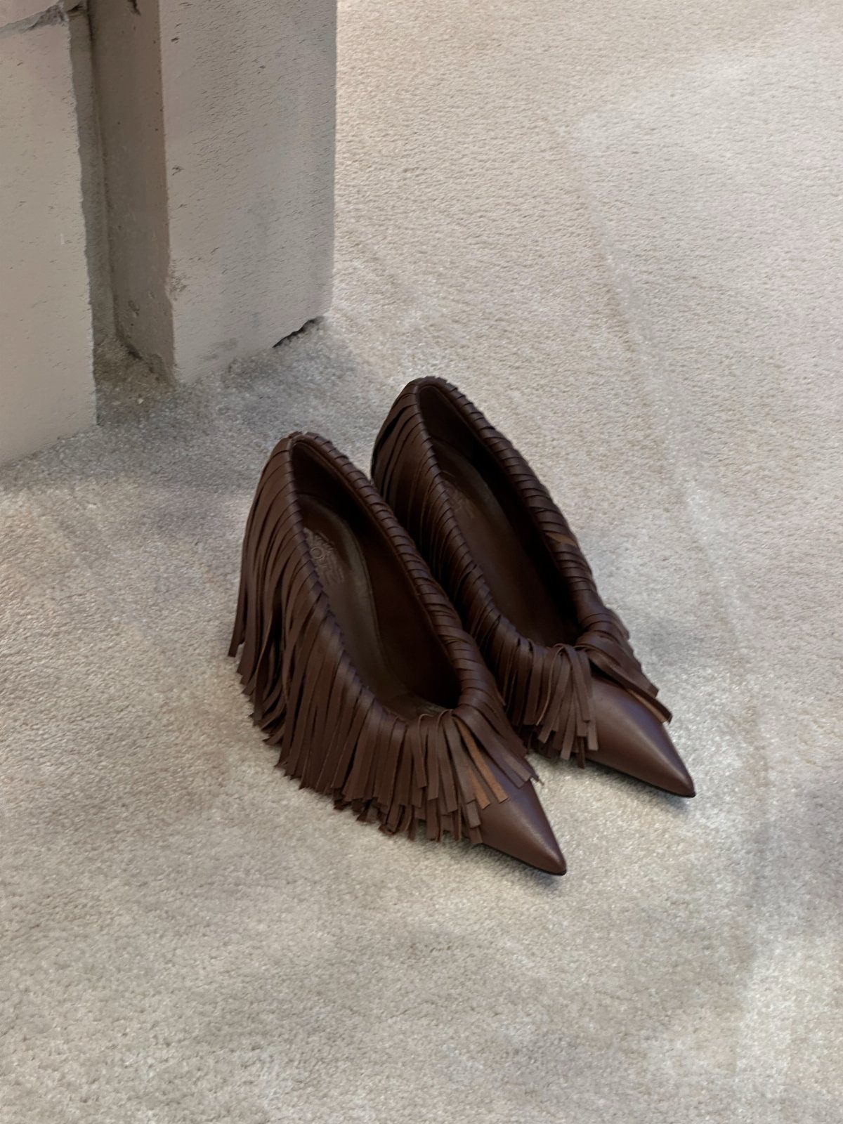 Brown leather pumps with long fringe accents on a grey concrete floor
