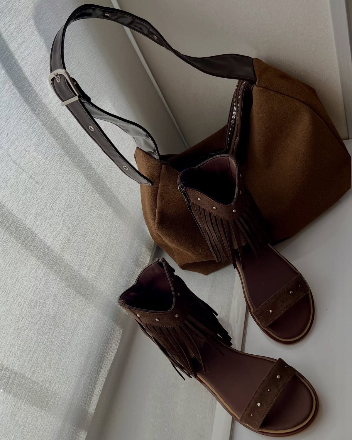 Brown suede fringe sandals and a matching brown suede handbag on a white surface.