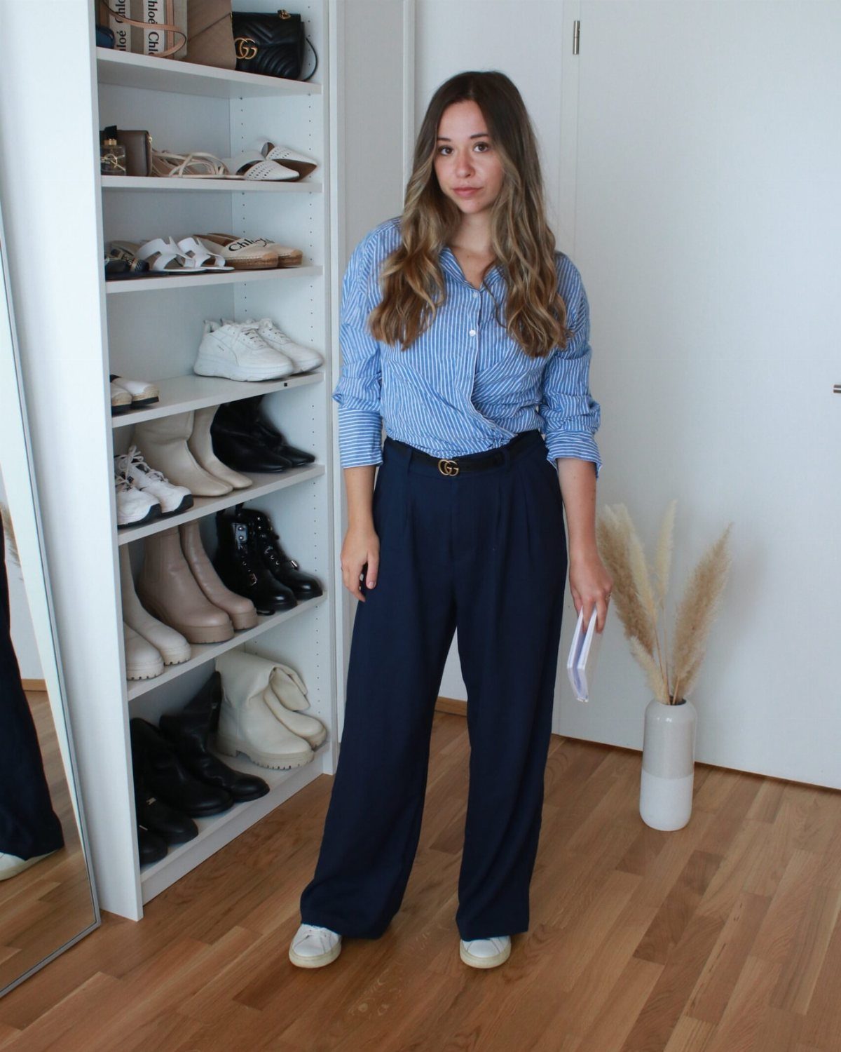 Woman wearing a striped blue shirt, navy wide-leg trousers, and white sneakers indoors.