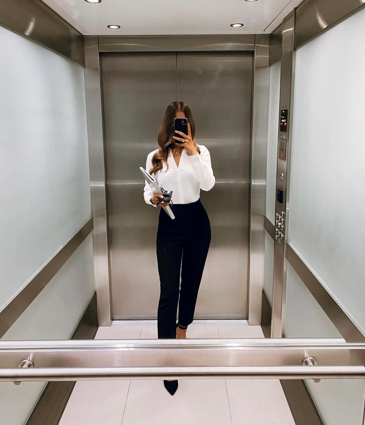 Woman in a white button-down shirt and black trousers posing in an elevator