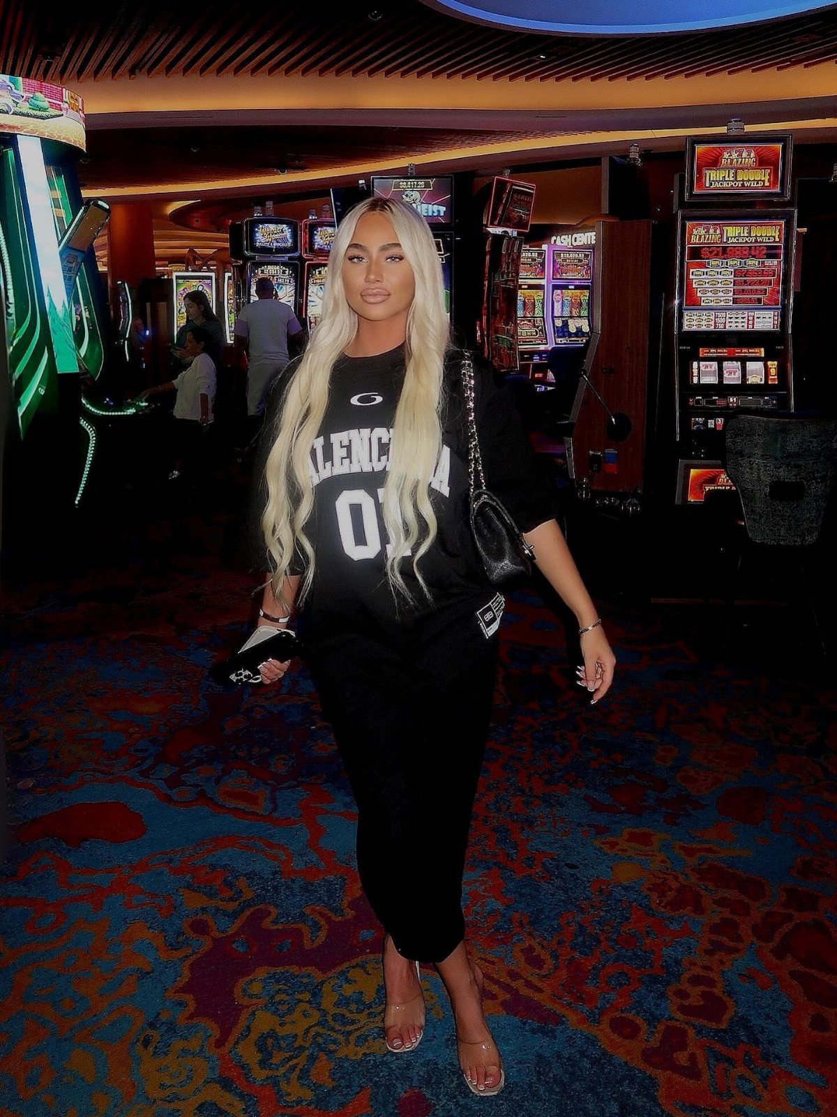 Woman in black casual outfit posing inside a casino with slot machines.