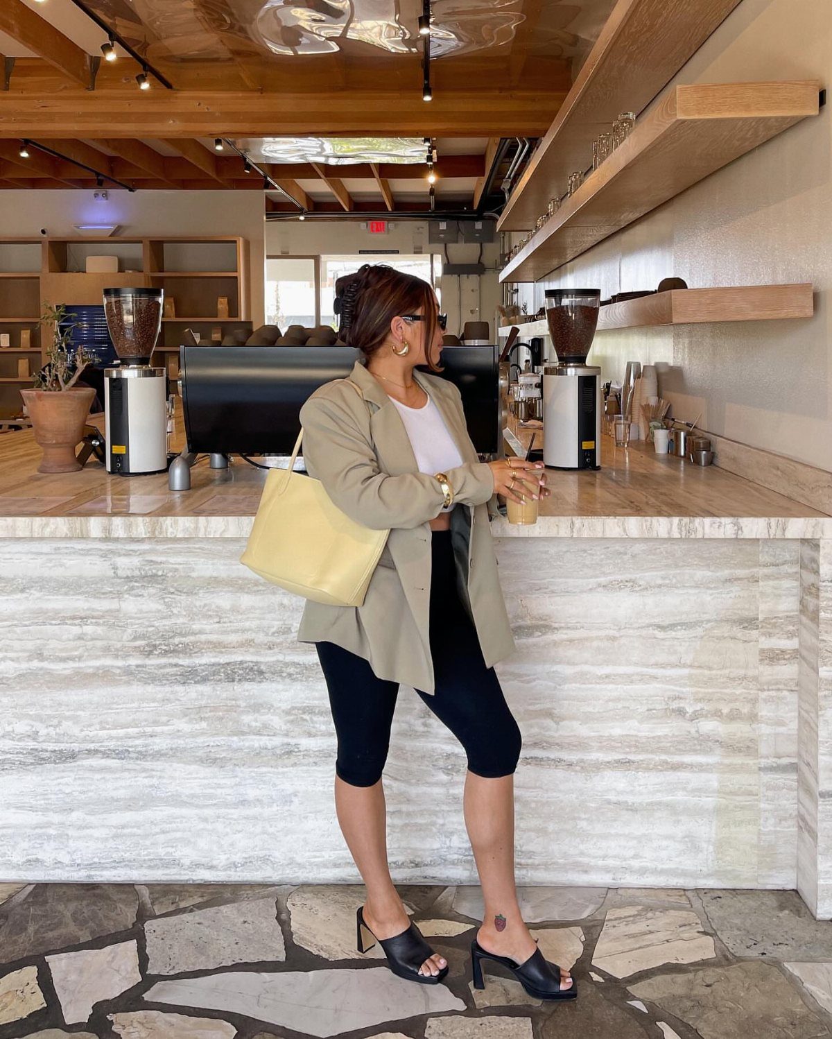 12 Casual Elegance Outfits for Easy Everyday Style 4 Woman in beige cropped blazer, white tank top, and black capris in a cafe.