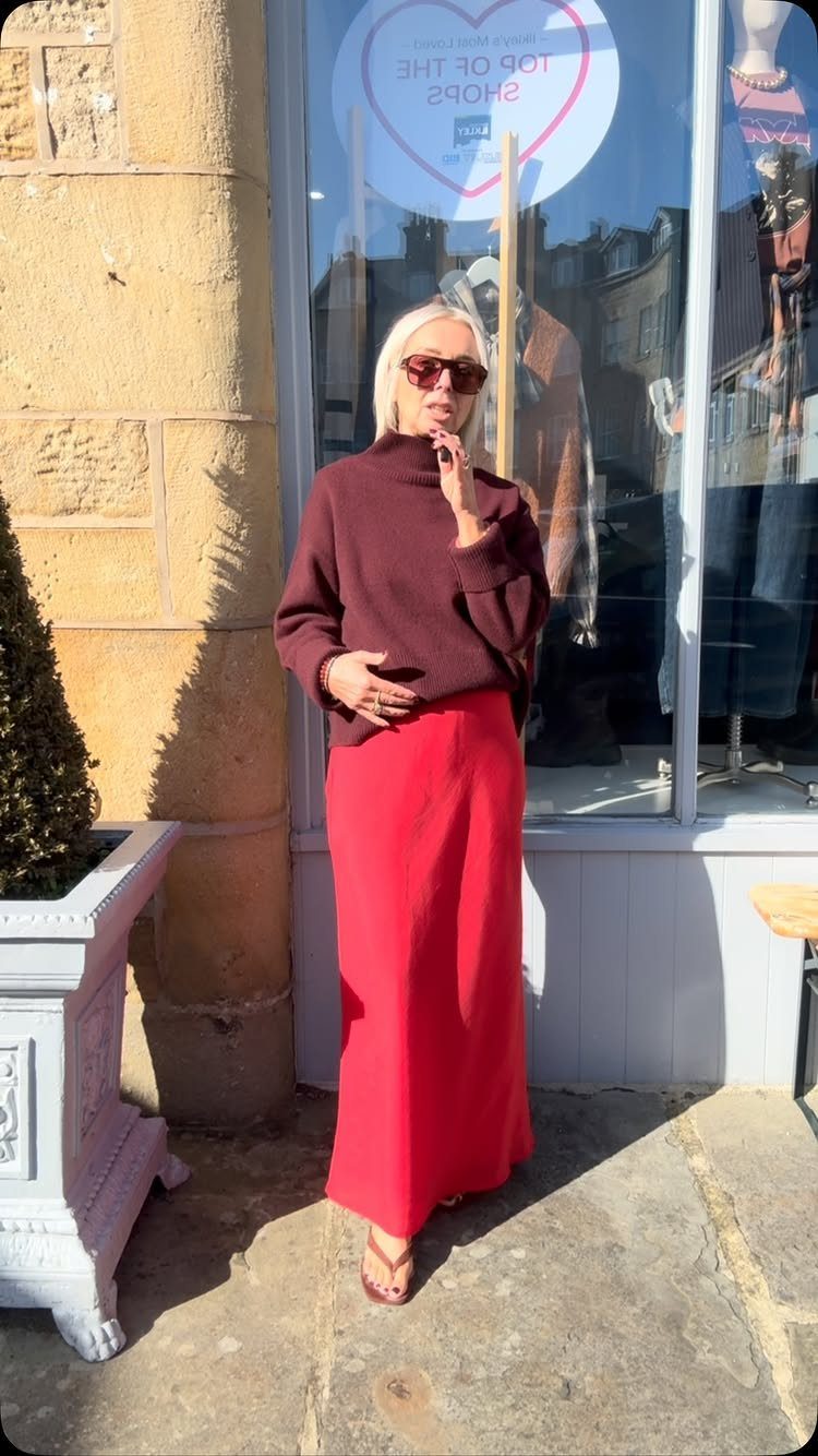 12 Casual Elegance Outfits for Easy Everyday Style 1 Woman wearing a burgundy turtleneck sweater and long red satin slip skirt outdoors.