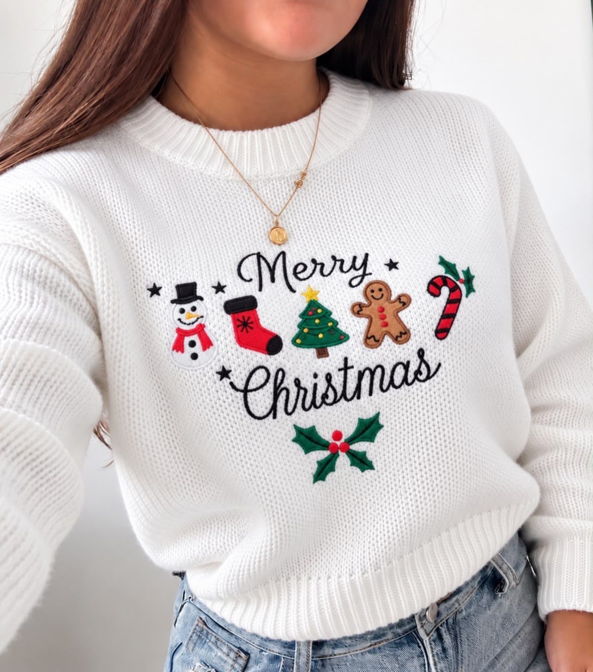 Christmas Outfit for Work: 13 Ideas to Wear to the Office 6 White knit Christmas sweater with festive icons and text paired with blue jeans.