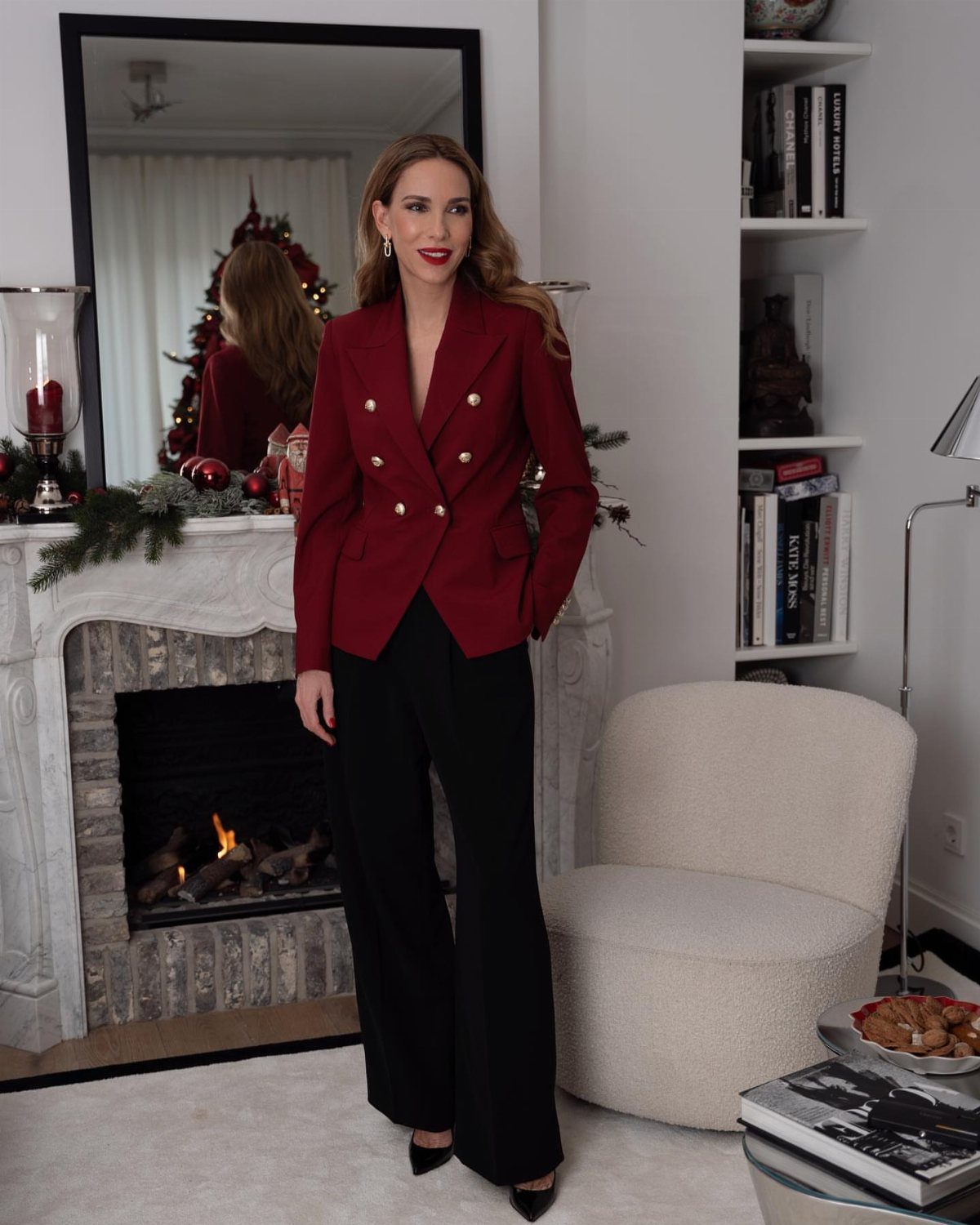 Christmas Outfit for Work: 13 Ideas to Wear to the Office 4 Woman wearing a red tailored blazer and black wide-leg trousers in a festive room.