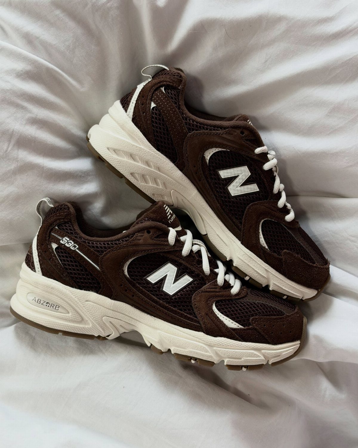 5 Chunky Shoes and New Balance Sneakers Worth Wearing 2 Brown and white New Balance 530 sneakers on a white wrinkled fabric background.