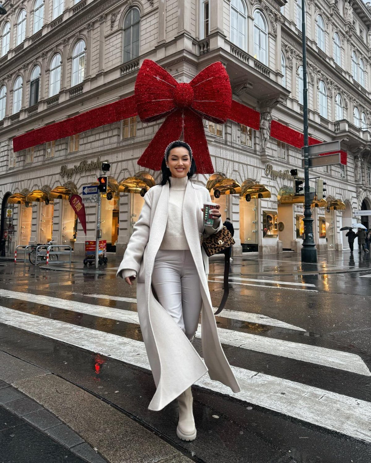 Woman in white cable knit sweater and coat standing before a giant red bow.